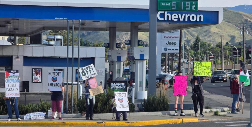Photo of eight protesters standing outside of the Wenatchee Chevron gas station holding up signs